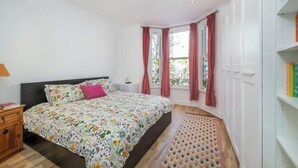 Un dormitorio con cama, mesita de noche, estantería y ventana con cortinas.