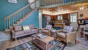 A spacious living area with a staircase, leather sofas, a coffee table, and a kitchen in the background.