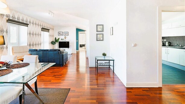 A modern living room with a glass dining table, a sofa, and a TV. There is a kitchen visible through an open door. - Downtown River Side by Homing (Lisbon)