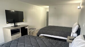 Ett hotellrum med en stor säng, en platt-TV som är monterad på ett träskåp, en mikrovågsugn och ett litet bord med en lampa.