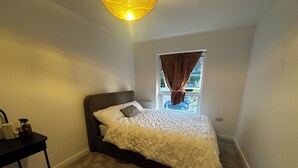 A bedroom with a bed, a window with curtains, a bedside table, and a chair.
