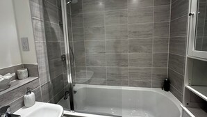 A modern bathroom with a glass-enclosed shower, a white bathtub, and a marble-tiled wall.