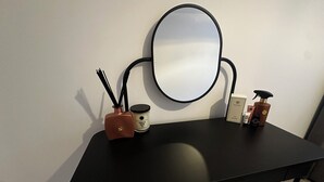 A black table with a round mirror, a small vase with black sticks, a vanilla bean candle, and a few personal care items.