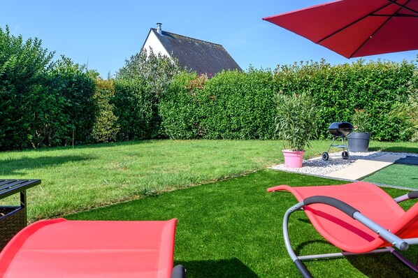 Un jardín bien cuidado con césped, una parrilla y un paraguas rojo.