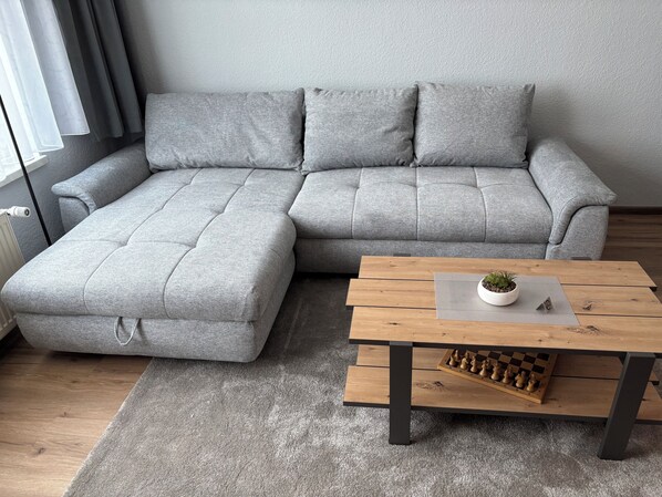 Un canapé d’angle gris, une table basse en bois et un jeu d’échecs.