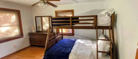 Dormitorio con literas, ventilador de techo, piso de madera, cómoda y ventana con persianas.