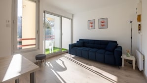 A modern living room with a sofa, a table, and a chair. There is a large window with a view of a garden.