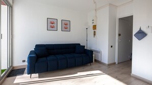 A modern living room with a dark blue sofa, a large window, and two framed pictures on the wall.