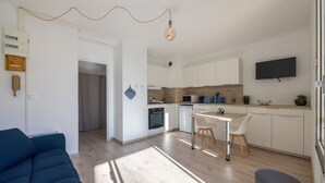 A modern kitchen with white cabinets, a dining area with a table and chairs, and a TV mounted on the wall.