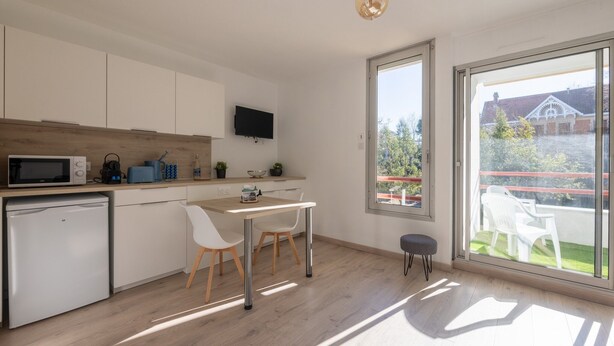 A modern kitchen with white cabinets, a microwave, a coffee maker, and a dining area with a table and chairs.