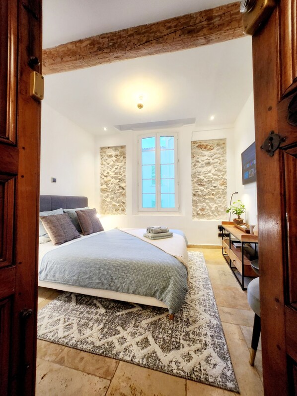 Ein Schlafzimmer mit einem Bett, einem Nachttisch, einer Kommode, einem Fenster und einer Steinwand.