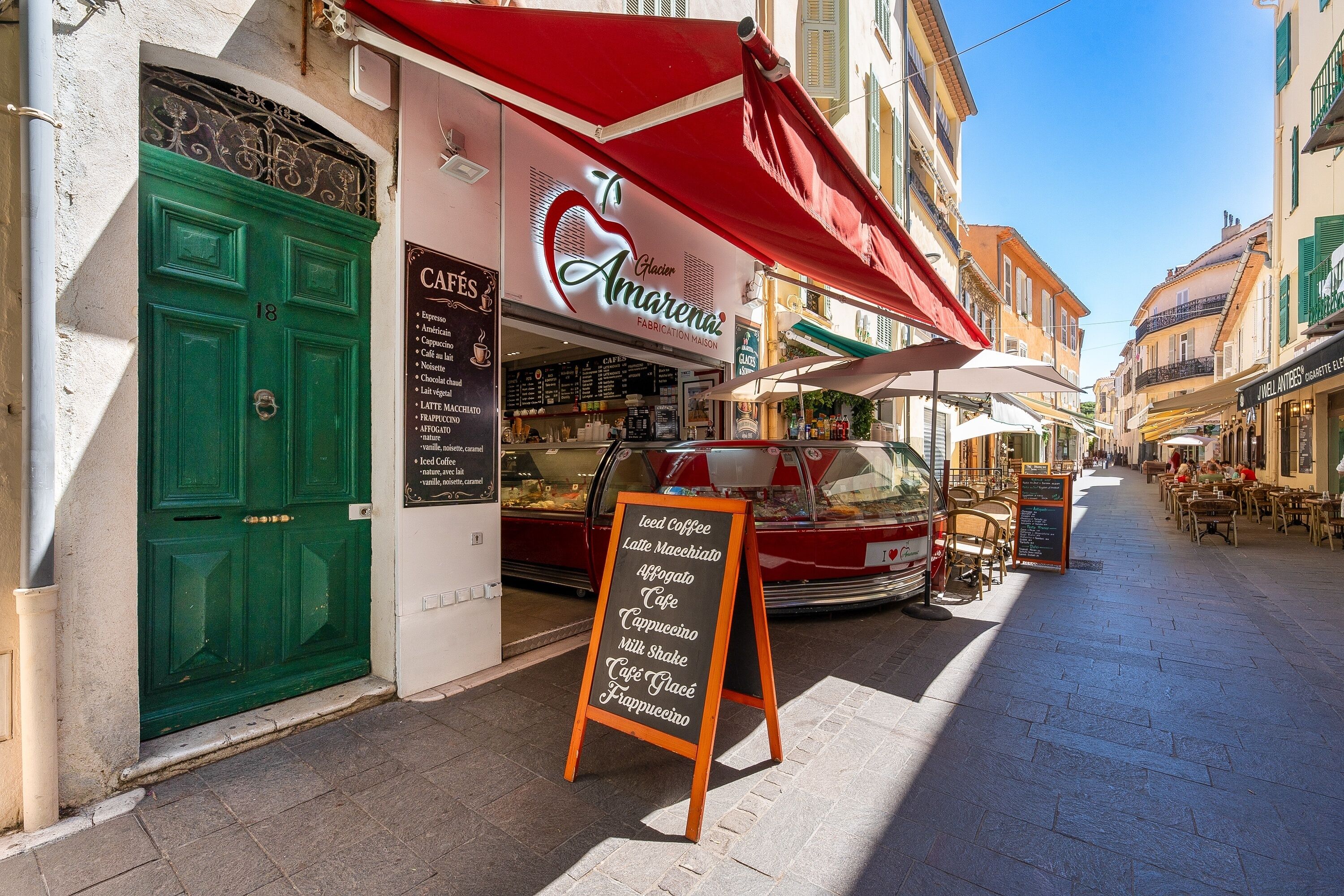 Une rue où se trouve un café appelé « Amarena » et où un panneau affiche une liste des plats et boissons proposés, comme du café et des milkshakes.