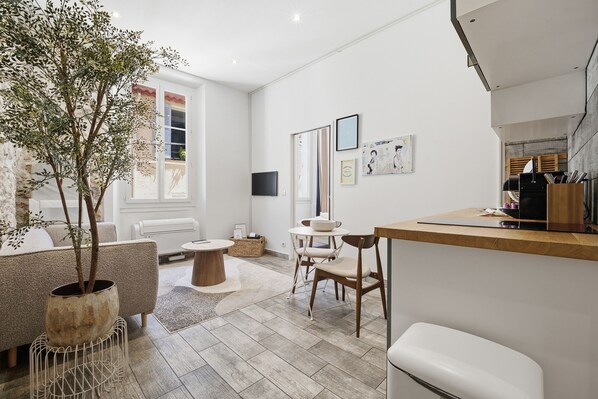 A modern living room with a sofa, a dining table, and a coffee table. There is a potted plant and a TV mounted on the wall.