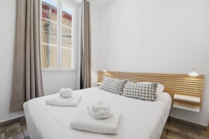 A hotel room with a bed, two pillows, a bedside table, a lamp, and a window with curtains.