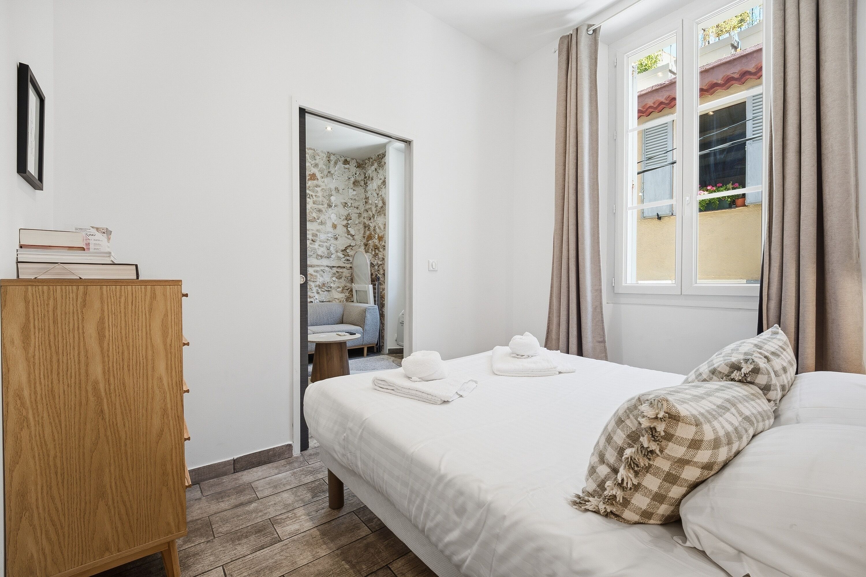Une chambre à coucher comprenant un lit, une commode en bois, une fenêtre avec des rideaux et une porte donnant sur une autre pièce.