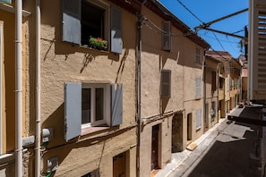 A narrow street with buildings featuring traditional architecture, shutters, and visible electrical wiring.