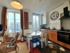A modern kitchen with a dining area, large windows, and a clock on the wall. - L'Amiral Barnaud - Appt proche de la plage (Antibes)