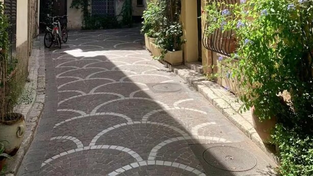 Una estrecha calle empedrada con edificios a ambos lados, una bicicleta estacionada a la izquierda y una reja a la derecha.