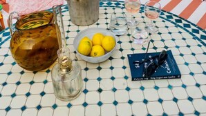 Terraza en la azotea con una mesa redonda preparada para dos personas, que incluye una jofaina de metal, una botella, un cuenco de limones y un par de gafas de sol.