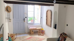 Una sala acogedora con un sofá blanco, una mesa de centro redonda de mimbre y un pequeño banco de madera. Un tapete colorido está en el suelo, y una cesta de mimbre se encuentra cerca del banco.