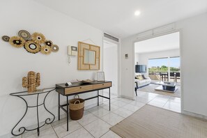 A modern interior with a glass console table, a woven basket, a mirror, and a view to an outdoor seating area.
