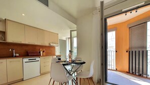 Una cocina moderna con armarios blancos, lavavajillas y un comedor con mesa de vidrio y sillas blancas.