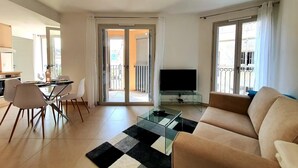 Una sala de estar con un sofá, un televisor, una mesa de centro de vidrio y un comedor con sillas y una mesa.