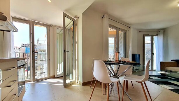 Un comedor moderno con una mesa de vidrio y sillas blancas, ventanas amplias y vistas a la ciudad.