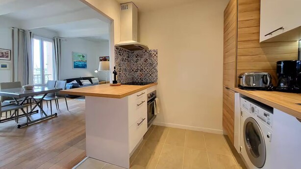 A modern kitchen with a central island, a built-in washing machine, and a dining area with a view. - L'Aiguillon Antibois - Proche Port (Antibes)
