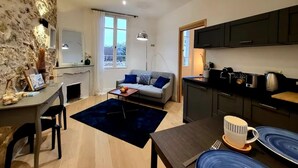 Un espacio habitable moderno con una pared de piedra, una zona de comedor con mesa y sillas, un sofá con cojines, una cocina con armarios y electrodomésticos, y un gran ventanal que proporciona luz natural.