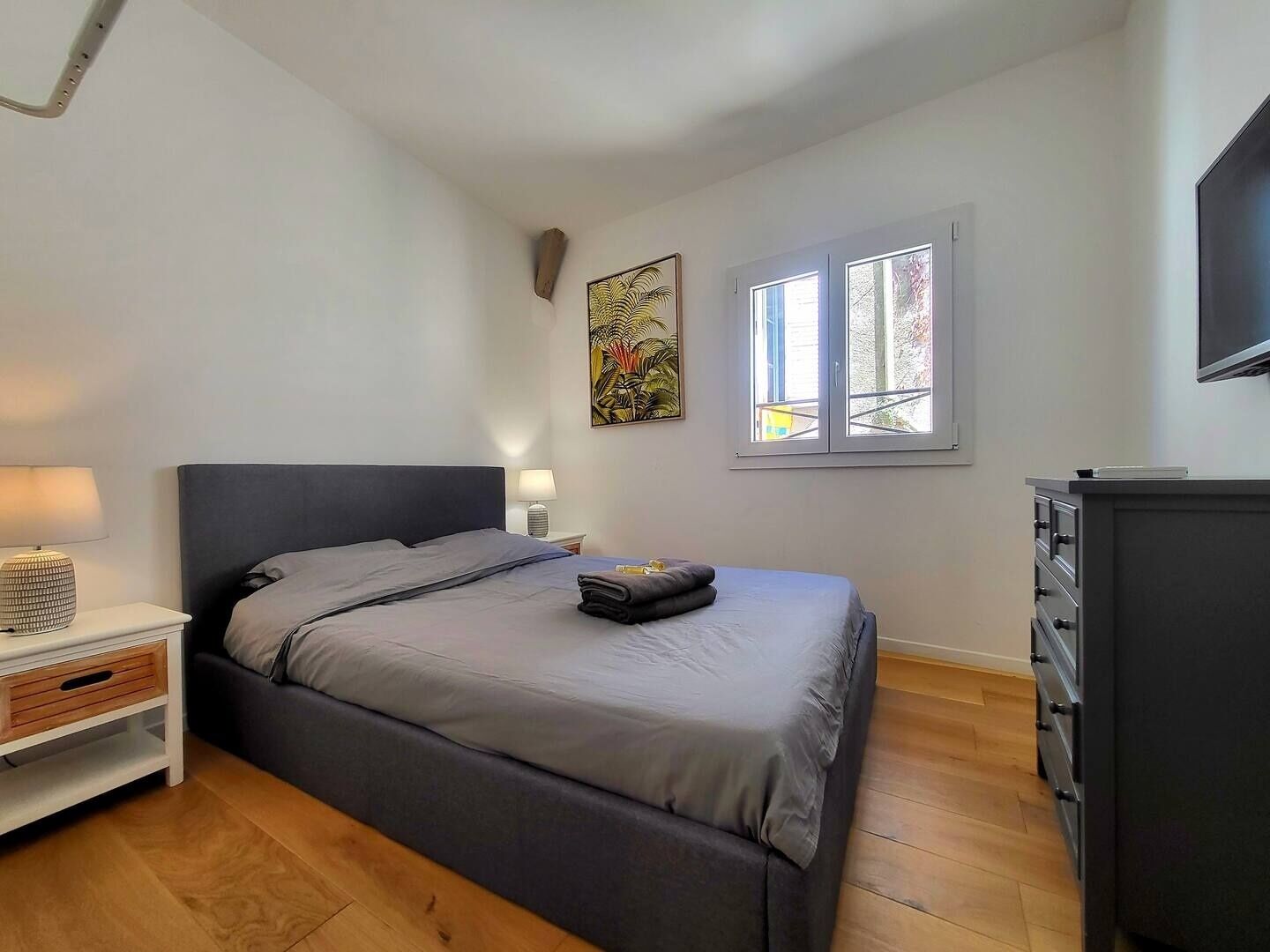 Een slaapkamer met een bed, nachtkastjes, een dressoir, een raam en een schilderij aan de muur.