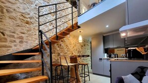 A modern kitchen with a stone wall, a wooden staircase, and a dining area with bar stools.
