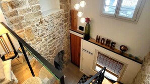 A cozy kitchen with a stone wall, wooden beams, a hanging light fixture, and a window with a view.