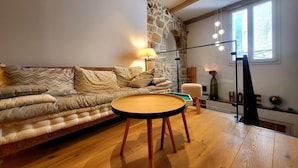 A cozy living room with a sofa, a round wooden coffee table, a lamp, and a stone wall.