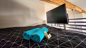 A room with a bed, a flat-screen TV, and a wooden ceiling beam. - Le Cosy Antibois - Proche Marché Provençal (Antibes)