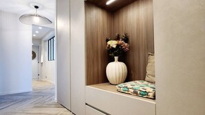 Un couloir doté d’un plancher en bois, un espace détente aménagé en alcôve avec un vase de fleurs et un luminaire suspendu.