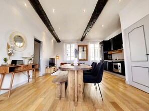 Un vaste espace de vie comprenant un coin repas avec une table en bois, des chaises noires, un téléviseur et une cuisine équipée d’appareils électroménagers modernes.