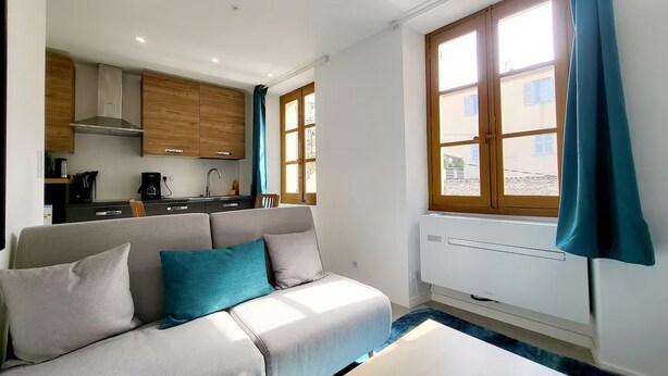 Un espacio habitable compacto con sofá, pequeña cocina y ventana con cortinas.