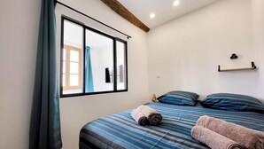 Un dormitorio con cama, ventana con cortinas, techo de vigas de madera y estante fijado a la pared.