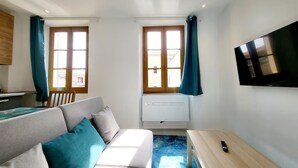 Un espace de vie compact comprenant un canapé, une petite table, un téléviseur et une fenêtre avec des rideaux.