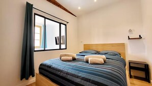 Une chambre avec un grand lit, une tête de lit en bois et une fenêtre avec des rideaux.