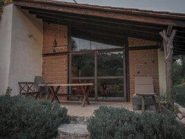 A rustic outdoor seating area with a wooden table and chairs, surrounded by greenery and a stone wall.