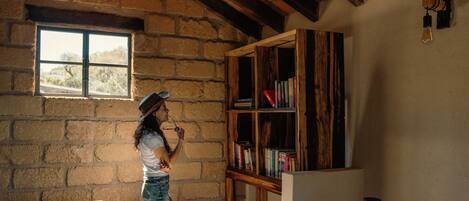 Una habitación rústica con pared de piedra, vigas de madera, una estantería y una ventana.