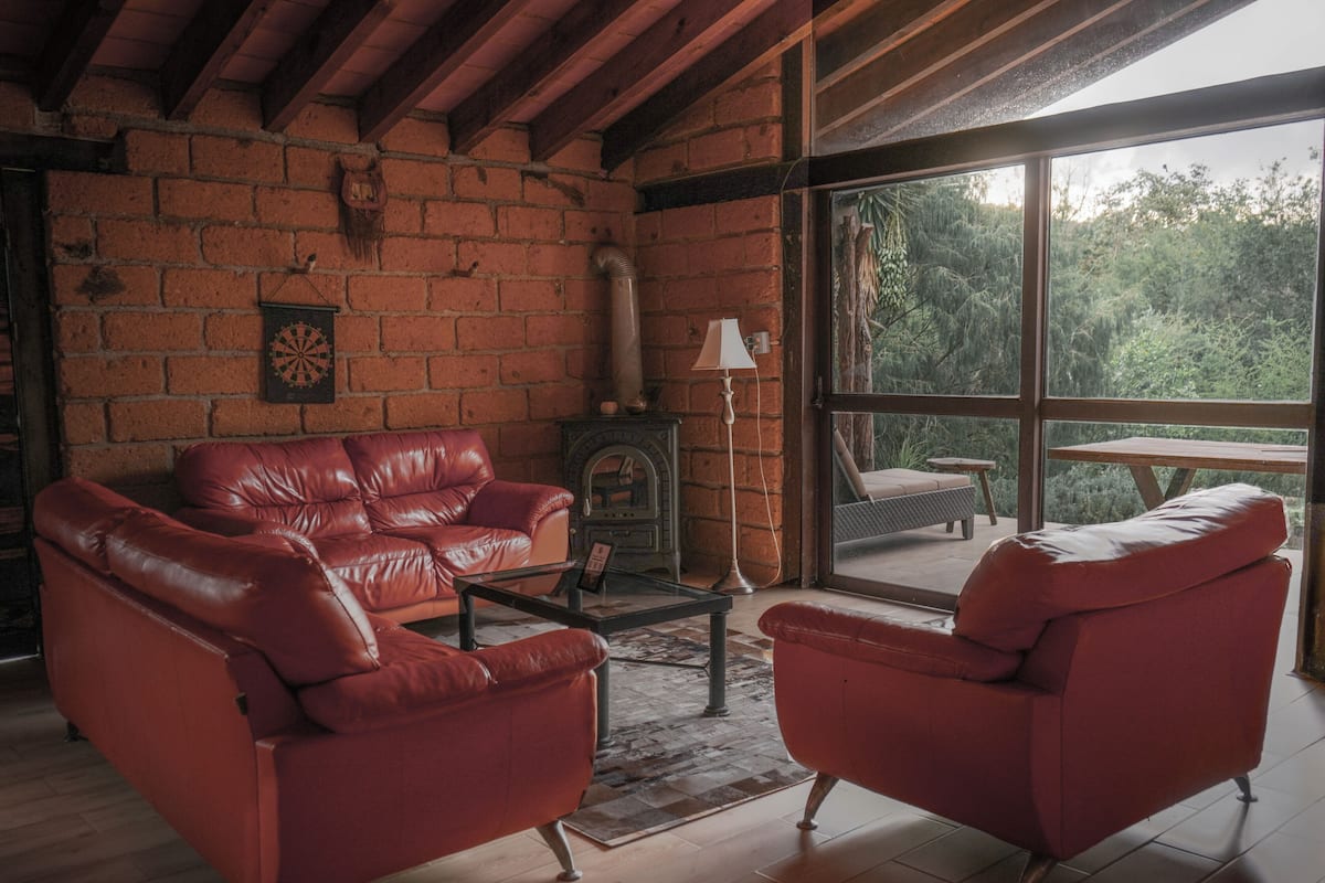 Ein gemütlicher Raum mit Backsteinwand, Kamin, Ledersofas und einem großen Fenster mit Blick ins Freie.