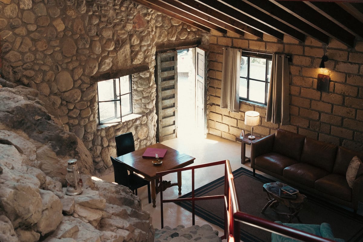 Ein rustikales Interieur mit Steinwänden, Holzbalken, einer Steintreppe, einem Holztisch und einem Ledersofa.