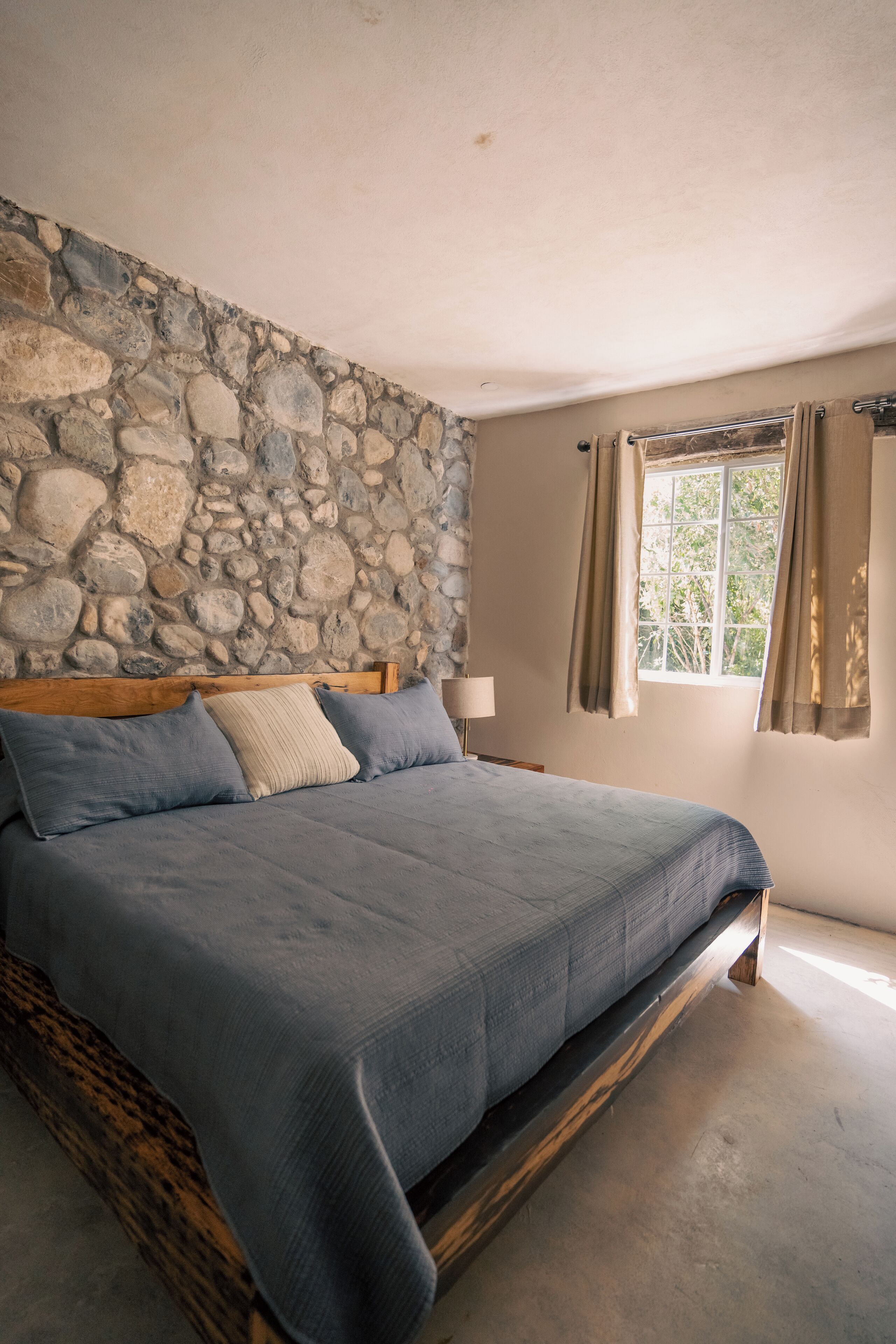 A bedroom with a stone wall, a bed with a wooden frame, and a window with curtains.