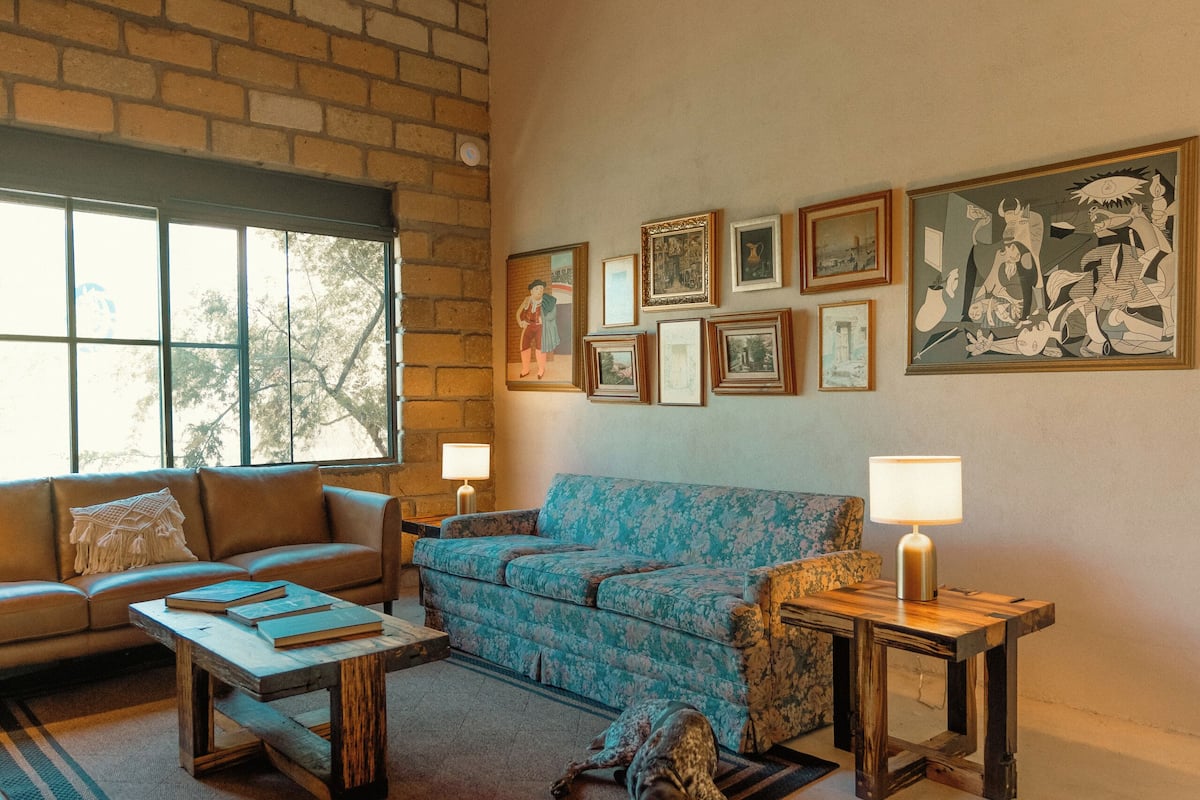 Ein gemütliches Wohnzimmer mit Ziegelwand, großem Fenster und einem blau gemusterten Sofa.