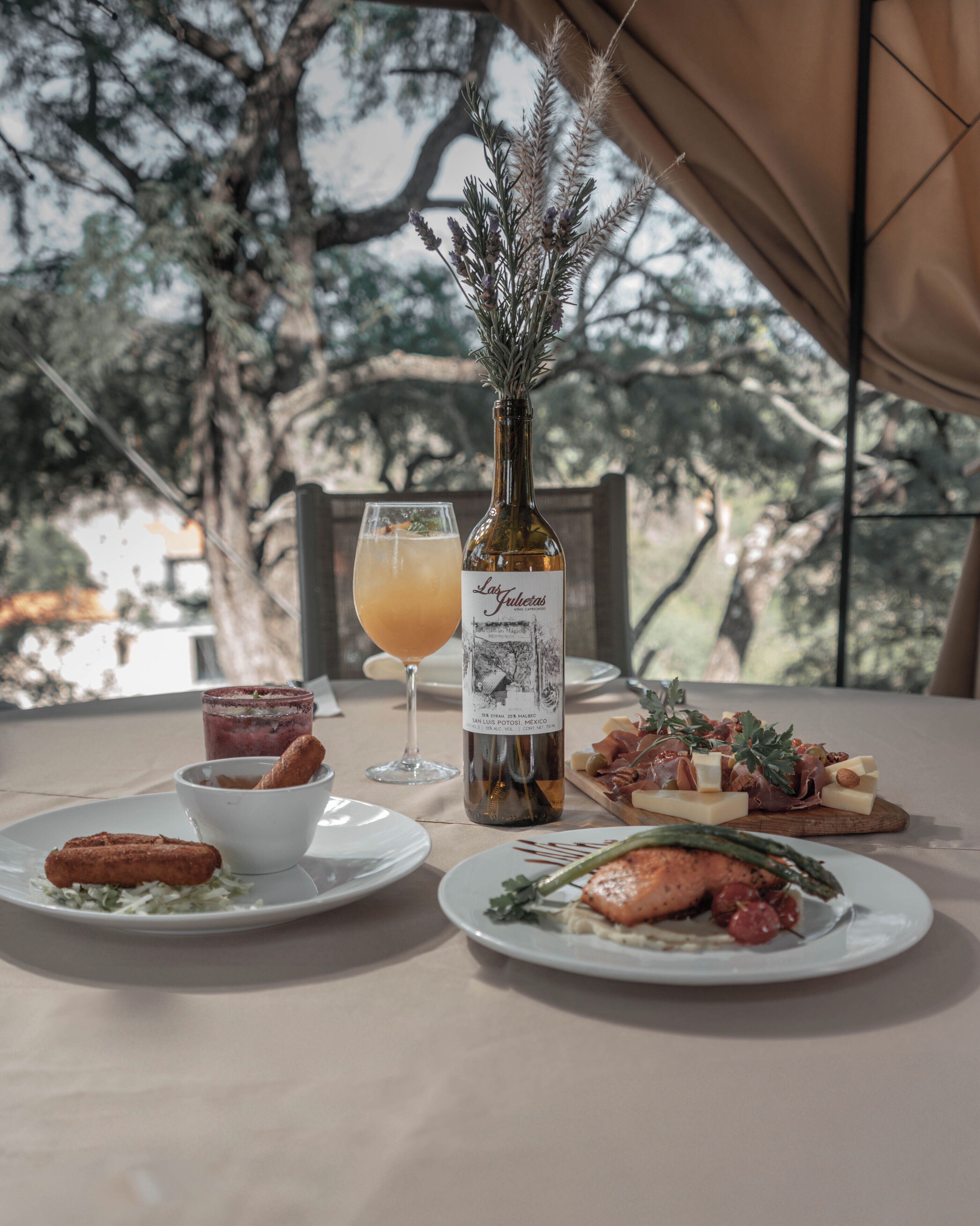 A table set with a bottle of wine, a glass of juice, and plates of food including salmon and cheese.