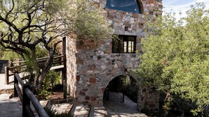 A stone building with a large arched window and a wooden door. - Armadillo Mágico (Armadillo de los Infante)