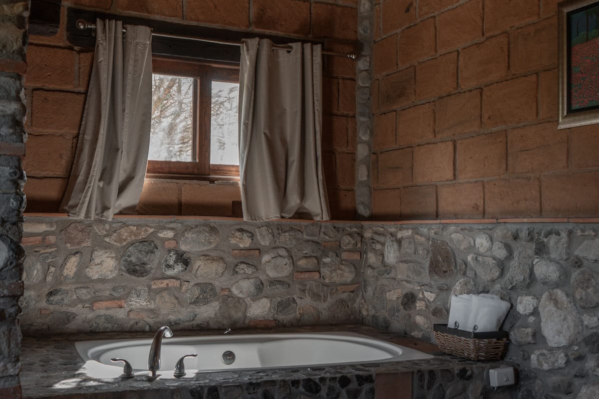 Eine SteinsBadewanne mit Fenster darüber, Vorhängen und einem Korb mit Handtüchern.